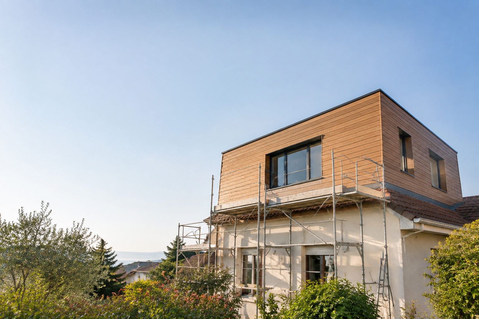 Maison en cours de surélévation avec un étage en bois moderne entouré d'échafaudages sous un ciel bleu clair.